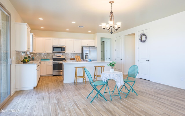 kitchen featuring a center island, stainless steel appliances, light wood-type flooring, and a notable chandelier