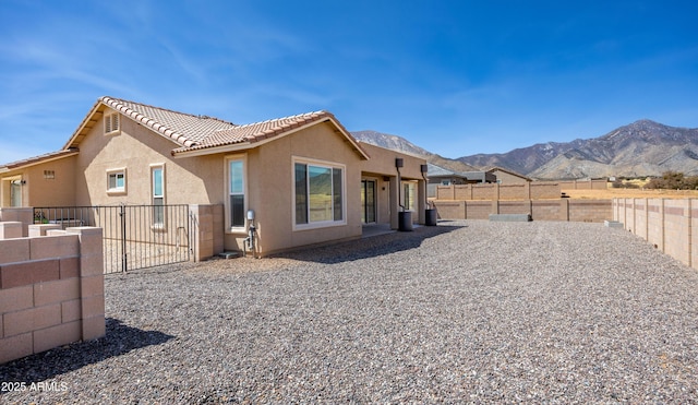 back of house featuring a tiled roof, a gate, a mountain view, a fenced backyard, and stucco siding