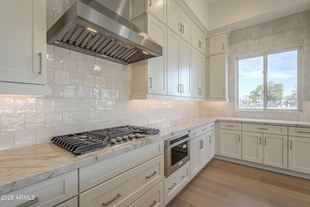 kitchen with stainless steel gas cooktop, light stone counters, island range hood, light wood-type flooring, and backsplash