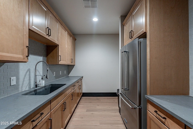 kitchen with tasteful backsplash, high end fridge, sink, and light hardwood / wood-style flooring