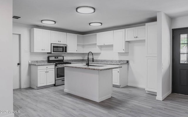 kitchen with white cabinetry, an island with sink, stainless steel appliances, light wood-type flooring, and sink