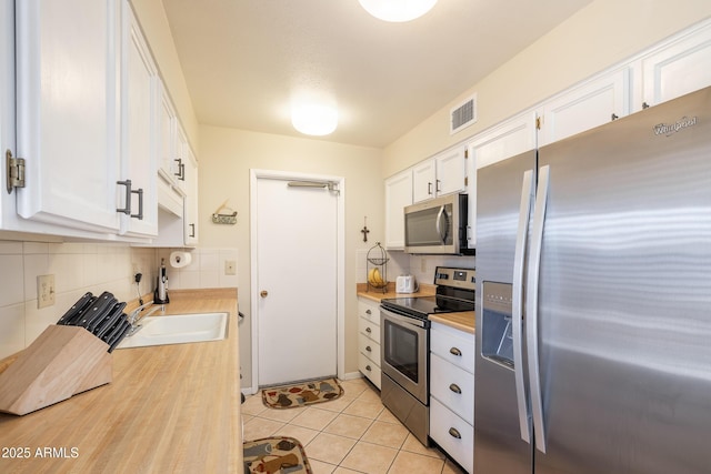 kitchen featuring white cabinetry, stainless steel appliances, decorative backsplash, sink, and light tile patterned floors