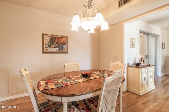 dining area with a notable chandelier, a textured ceiling, and light hardwood / wood-style floors