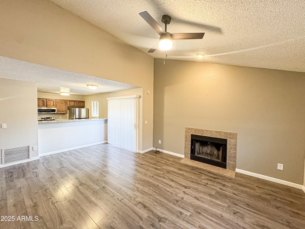 unfurnished living room with light wood-type flooring, a textured ceiling, vaulted ceiling, ceiling fan, and a fireplace