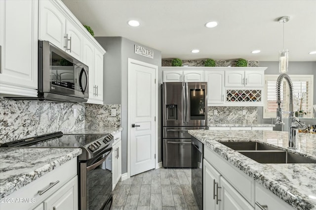 kitchen featuring light stone counters, white cabinetry, stainless steel appliances, and a sink