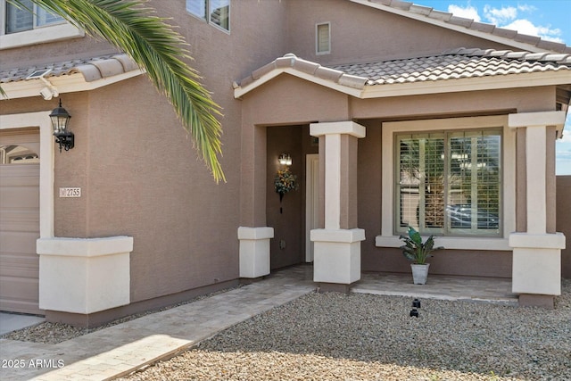 doorway to property featuring a garage, a tile roof, and stucco siding