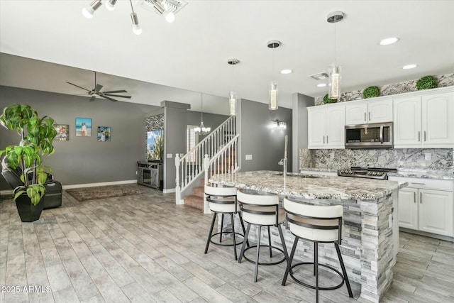 kitchen featuring light wood finished floors, stainless steel microwave, visible vents, decorative backsplash, and range