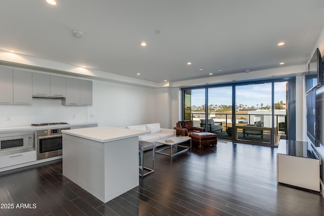 kitchen featuring a center island, gas cooktop, oven, white microwave, and backsplash