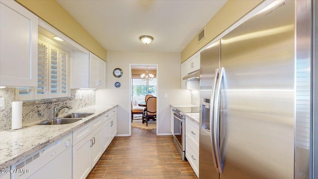 kitchen featuring light stone counters, appliances with stainless steel finishes, a notable chandelier, hardwood / wood-style floors, and white cabinets