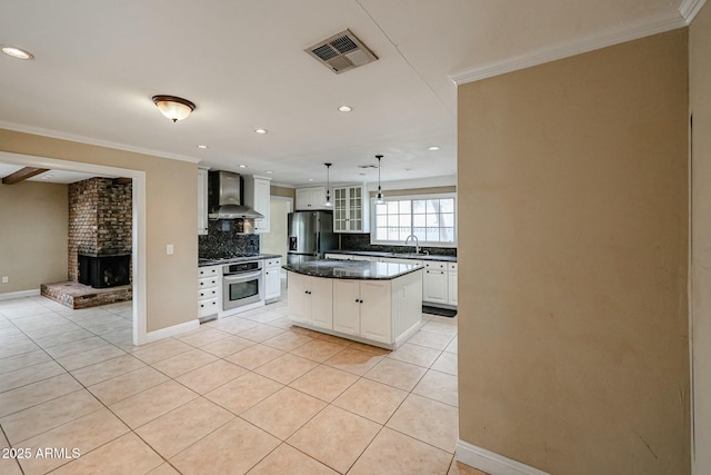 kitchen with visible vents, dark countertops, wall chimney exhaust hood, appliances with stainless steel finishes, and white cabinetry