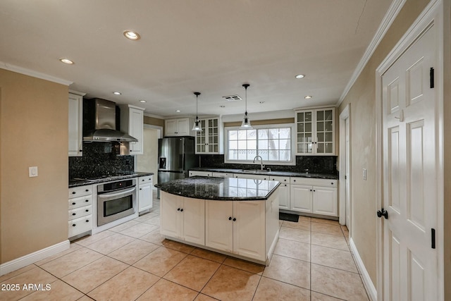 kitchen featuring a sink, wall chimney range hood, appliances with stainless steel finishes, a center island, and glass insert cabinets