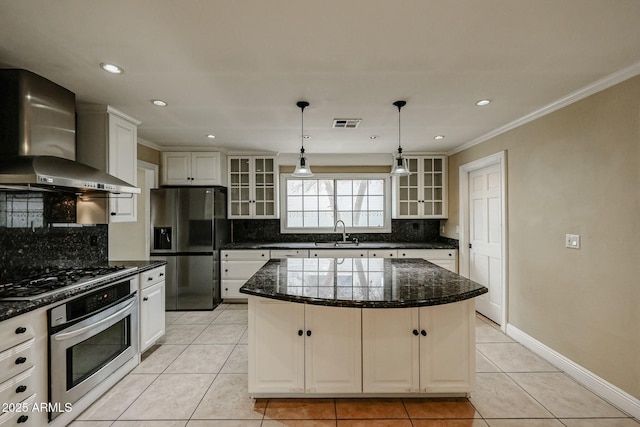 kitchen featuring appliances with stainless steel finishes, glass insert cabinets, white cabinetry, a kitchen island, and wall chimney exhaust hood