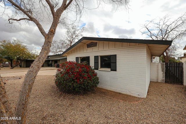 view of property exterior featuring brick siding, board and batten siding, and fence