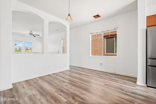 unfurnished dining area featuring visible vents, baseboards, ceiling fan, wood finished floors, and arched walkways