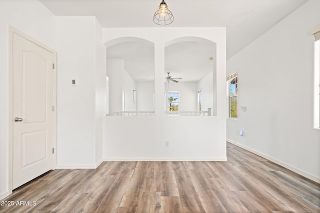 unfurnished room featuring baseboards, arched walkways, and wood finished floors