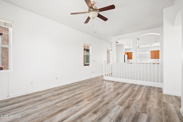 spare room featuring a ceiling fan, baseboards, light wood finished floors, arched walkways, and a sink