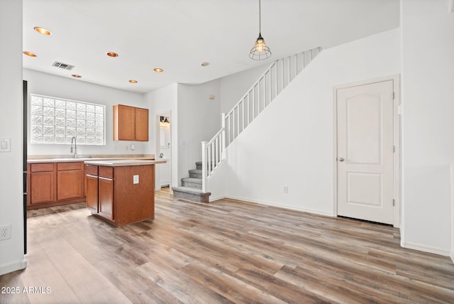 kitchen with light wood-type flooring, visible vents, brown cabinets, a sink, and light countertops