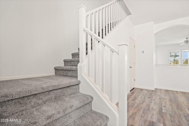 staircase featuring baseboards, wood finished floors, arched walkways, and ceiling fan