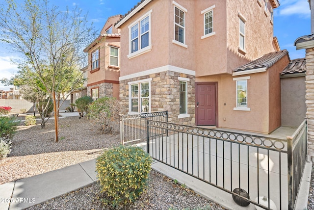 townhome / multi-family property featuring a fenced front yard, stone siding, stucco siding, and a tile roof