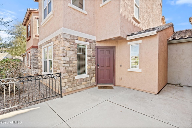 doorway to property featuring stone siding, stucco siding, and a tile roof