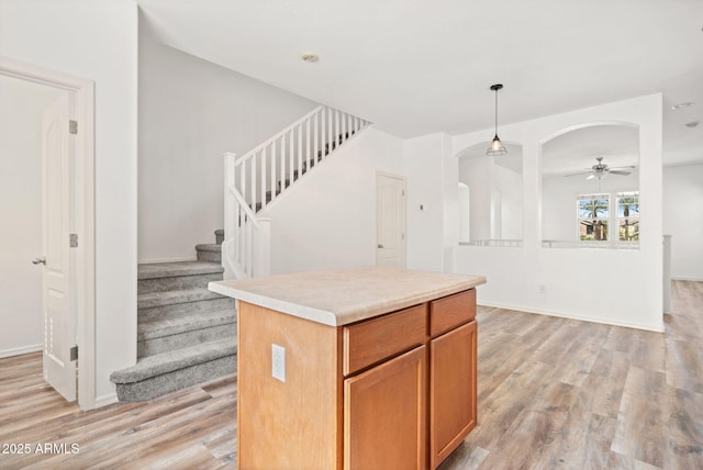 kitchen featuring light wood finished floors, a kitchen island, pendant lighting, arched walkways, and a ceiling fan