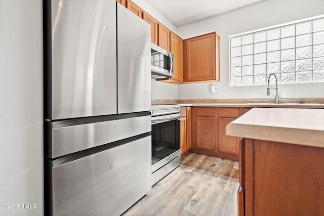 kitchen with brown cabinets, a sink, light wood-style floors, appliances with stainless steel finishes, and light countertops