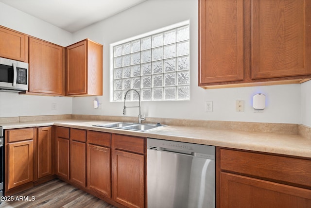 kitchen featuring wood finished floors, a sink, light countertops, appliances with stainless steel finishes, and brown cabinets