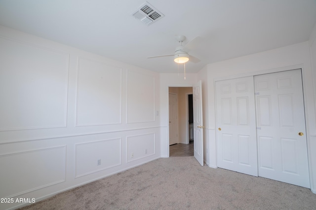 unfurnished bedroom featuring a decorative wall, a closet, visible vents, and carpet floors