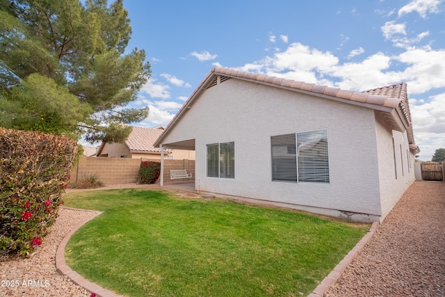 rear view of property with a tiled roof, a lawn, a fenced backyard, and stucco siding