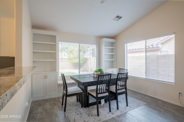 dining area with visible vents, wood finished floors, baseboards, and vaulted ceiling