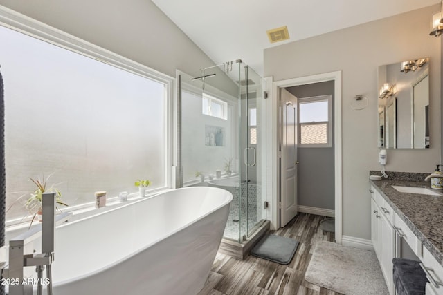 full bath with a freestanding bath, vanity, wood finished floors, visible vents, and a stall shower