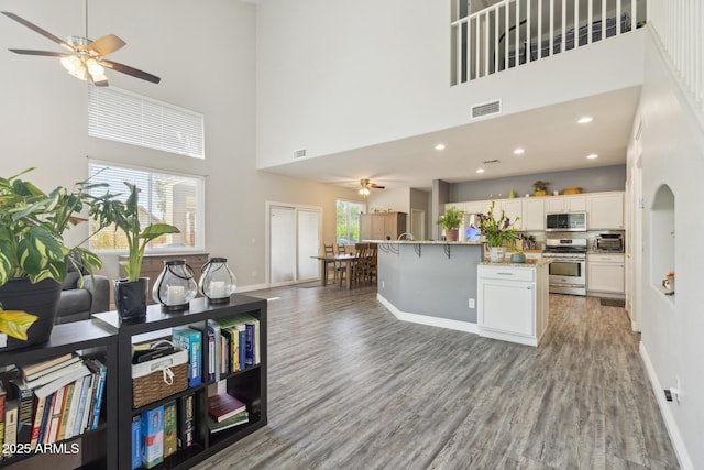 kitchen with ceiling fan, visible vents, a towering ceiling, stainless steel appliances, and light wood-style flooring