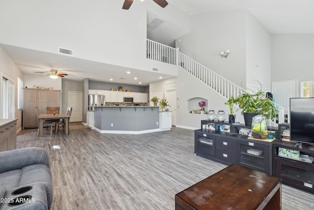 living area featuring light wood-style floors, ceiling fan, visible vents, and a towering ceiling