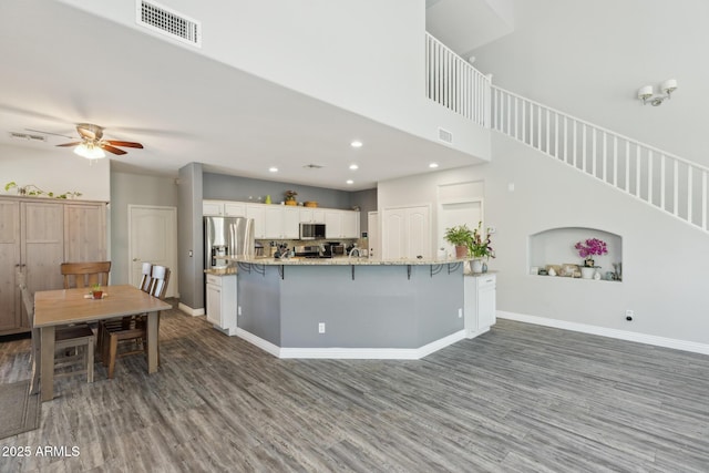 kitchen featuring visible vents, wood finished floors, a breakfast bar area, white cabinetry, and stainless steel appliances
