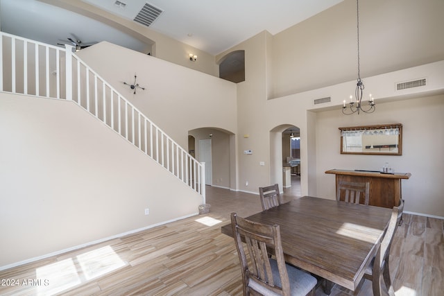 dining room with light hardwood / wood-style flooring, a towering ceiling, and ceiling fan with notable chandelier