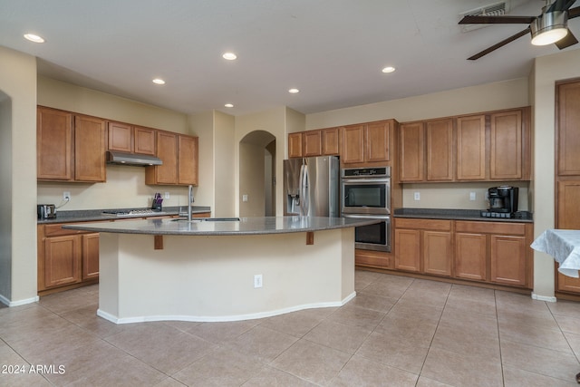 kitchen with appliances with stainless steel finishes, light tile patterned flooring, a kitchen bar, ceiling fan, and a kitchen island with sink