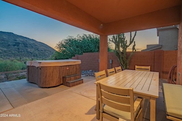 patio terrace at dusk featuring a mountain view and a hot tub