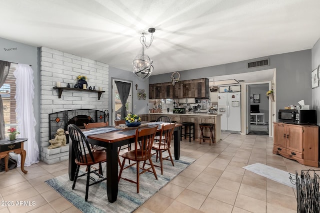 dining room featuring light tile patterned floors, visible vents, a chandelier, and a fireplace