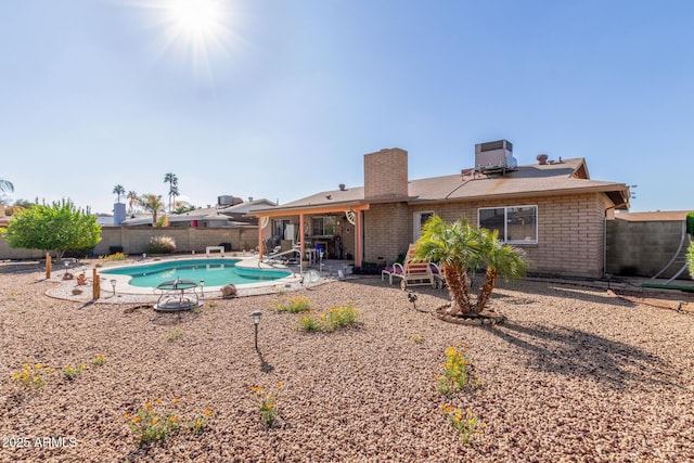 rear view of property featuring a fenced backyard, a fenced in pool, brick siding, a chimney, and a patio area