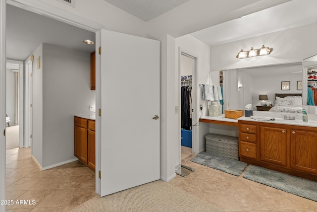 bathroom with a walk in closet, ensuite bathroom, vanity, baseboards, and tile patterned floors