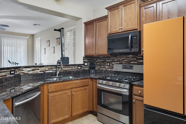 kitchen with visible vents, a sink, dark stone countertops, appliances with stainless steel finishes, and decorative backsplash