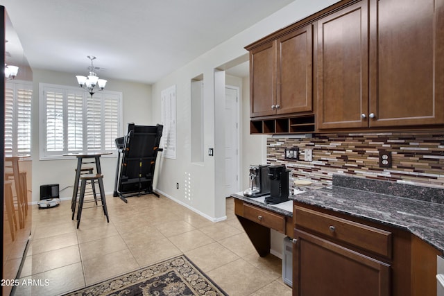 kitchen featuring dark stone countertops, tasteful backsplash, light tile patterned floors, baseboards, and a chandelier