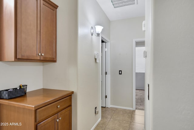 hall featuring light tile patterned floors, visible vents, and baseboards