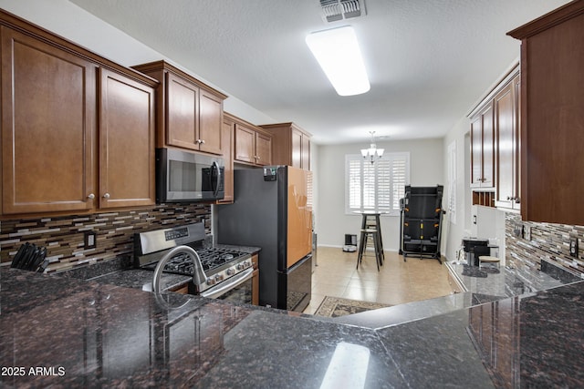 kitchen featuring tasteful backsplash, visible vents, dark stone counters, a notable chandelier, and stainless steel appliances