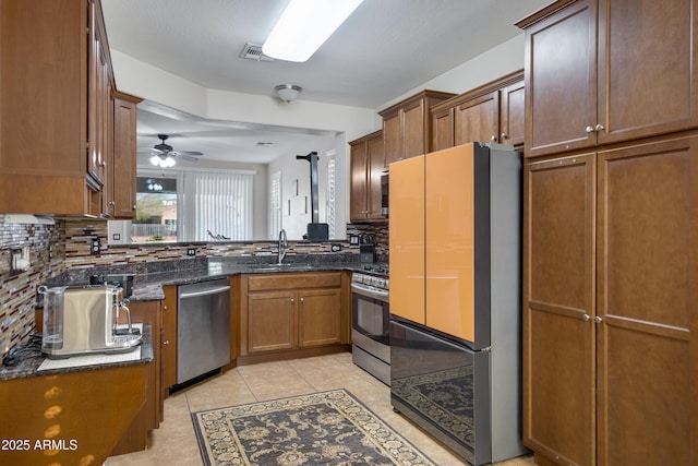 kitchen featuring tasteful backsplash, dark stone counters, light tile patterned floors, appliances with stainless steel finishes, and a sink