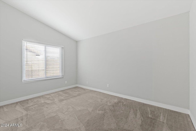 carpeted spare room with vaulted ceiling