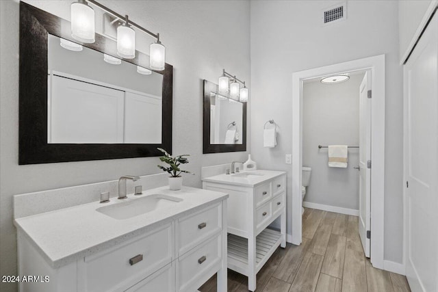 bathroom with toilet, dual bowl vanity, and hardwood / wood-style floors