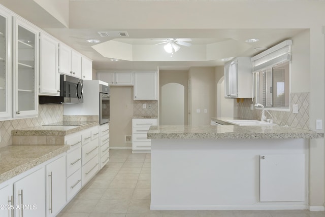 kitchen with ceiling fan, light tile patterned floors, appliances with stainless steel finishes, a tray ceiling, and white cabinetry