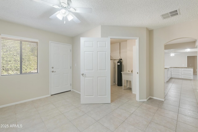 interior space with ensuite bath, ceiling fan, light tile patterned floors, and a textured ceiling