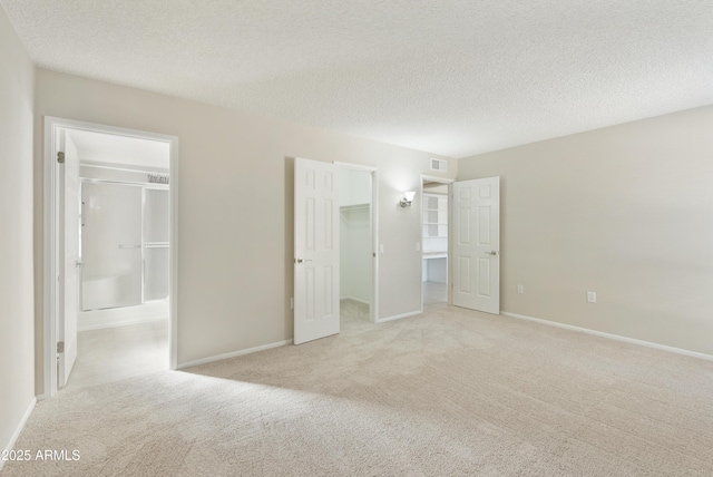 unfurnished bedroom with light carpet, a textured ceiling, a spacious closet, connected bathroom, and a closet